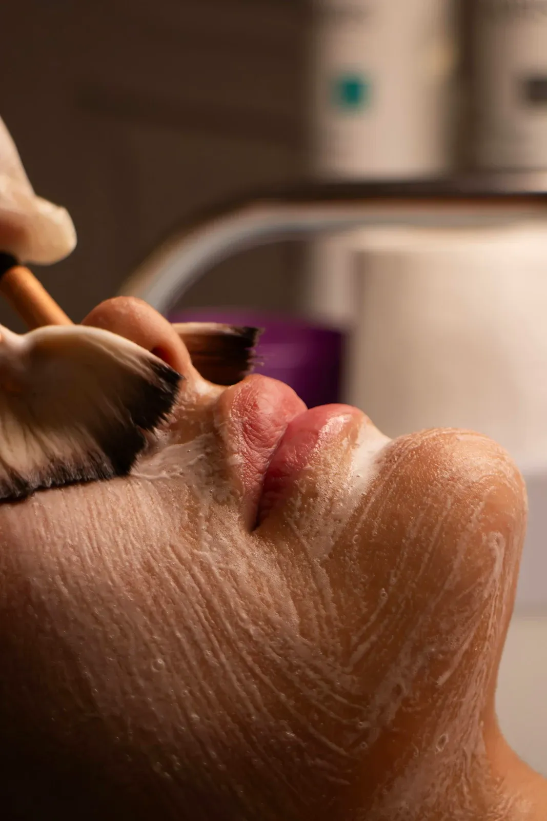 Pincel aplicando um creme branco no rosto de uma mulher madura durante um peeling químico